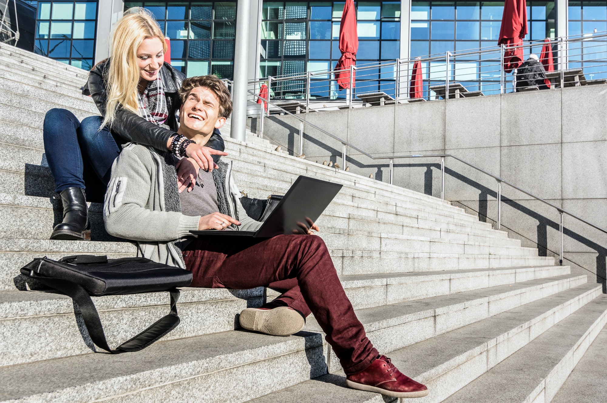 Hipster couple having fun using computer laptop in urban location on winter day